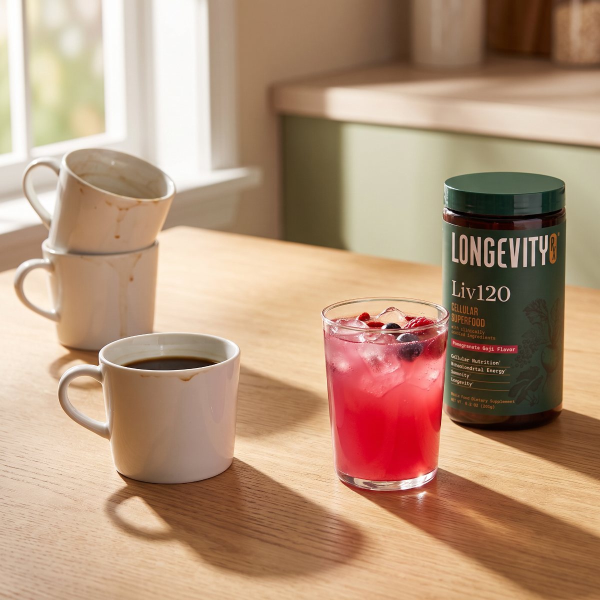 Three used coffee mugs on a wooden table beside a fresh glass of pink Liv120 and the Liv120 jar in afternoon light