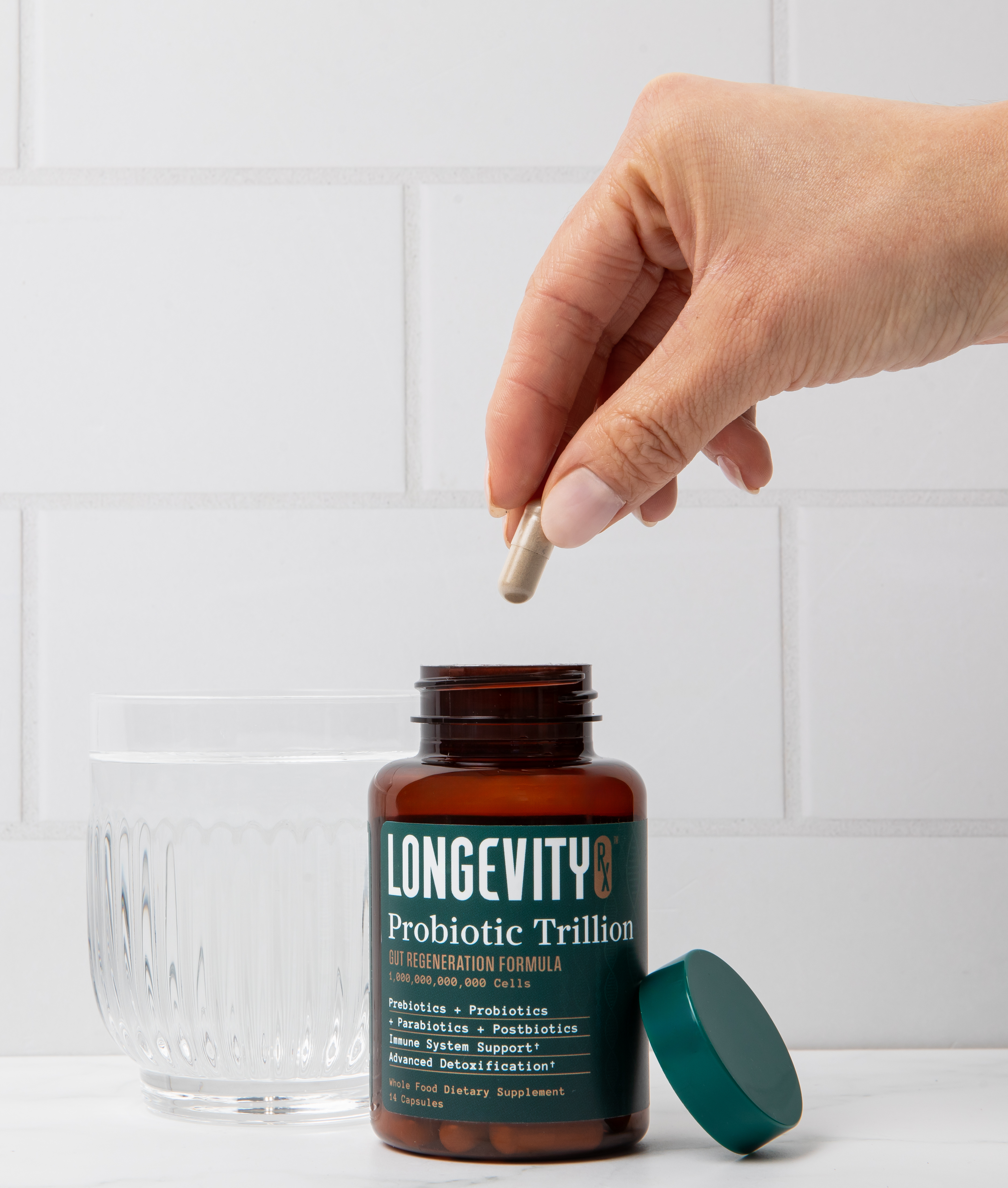 Hand holding a Probiotic Trillion capsule beside the bottle and a glass of water